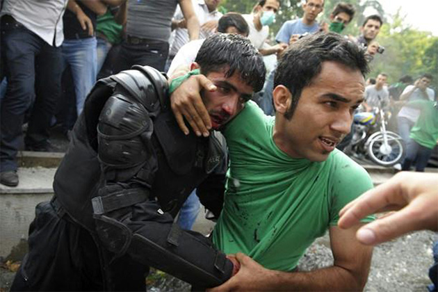 Civilians protect an Iranian police officer after he is beaten by rioters.