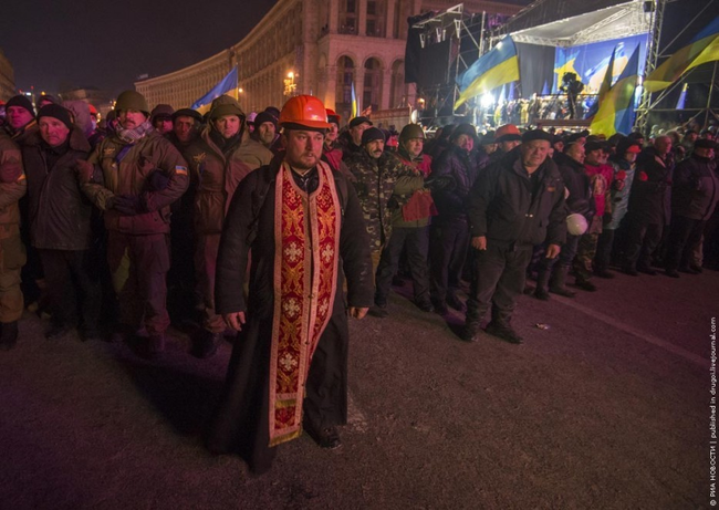 A priest acts as a human shield between protestor and police during protests in Ukraine in 2013.