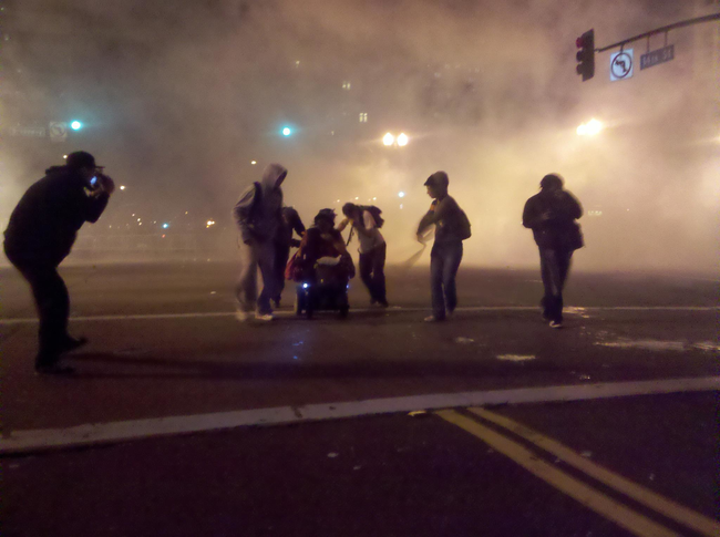 Protestors in Oakland, California, help a woman in a wheelchair get away from teargas.
