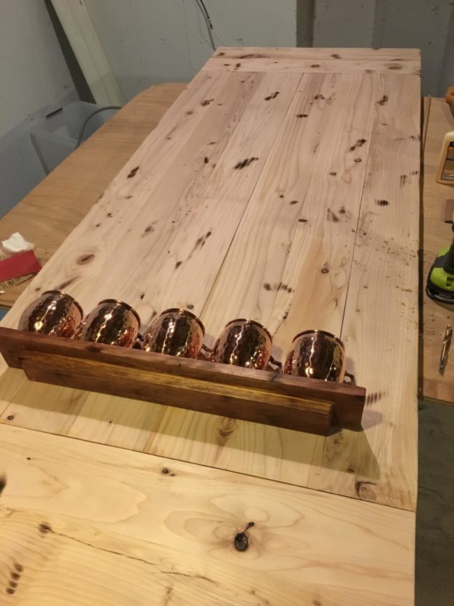 After using dowel rods and glue to mount a shelf toward the bottom, he arranged copper mugs on top where they'd catch the ping pong balls.